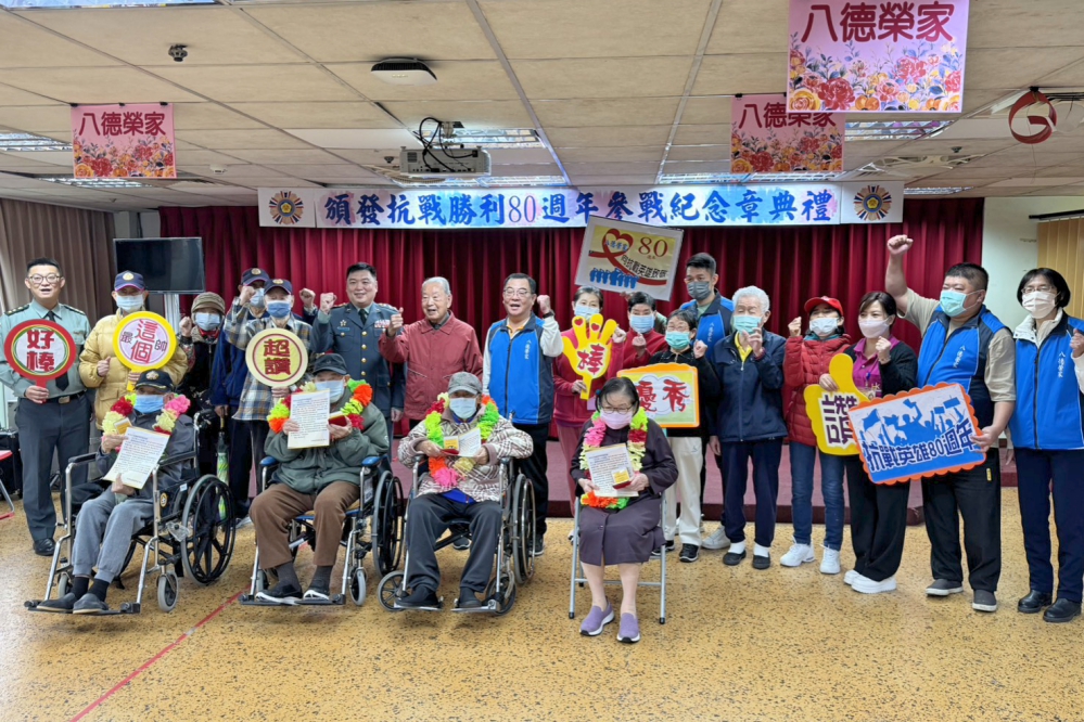八德榮家舉辦紀念抗戰勝利八十週年典禮蘇國棟上校後排左四與榮家幹部獲頒紀念章的長輩及工作人員手持標語開心合影場面溫馨_Fotor1 - 報新聞 Mega News
