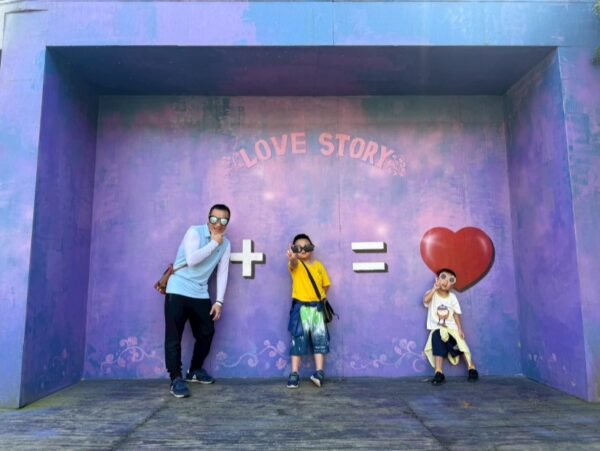 父子三人在壁畫前開心比手勢大笑，孩子露出燦爛笑容，能感受到與爸爸共度時光的喜悅。圖/台灣世界展望會